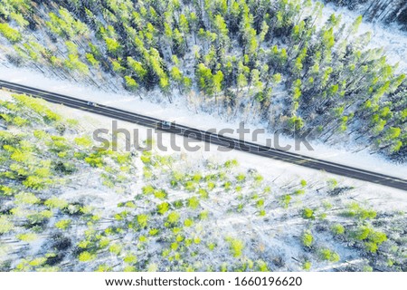 Aerial view of a winter country road in the forest with moving cars. Beautiful landscape. Captured from above with a drone. Aerial bird's eye road with car. Aerial top view forest. Texture of forest