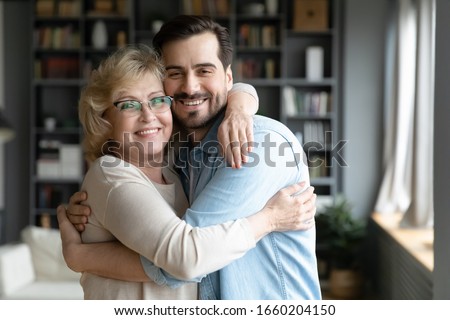 Portrait of smiling middle-aged mother hug cuddle adult son relax in living room together, happy senior 70s mom embrace grown-up man child enjoy family weekend reunion at home, bonding concept Royalty-Free Stock Photo #1660204150