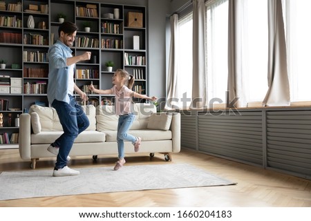 Happy little girl dancing with young father relaxing together in living room, overjoyed dad and small cute smiling preschooler daughter have fun moving listening to music at home, weekend concept Royalty-Free Stock Photo #1660204183
