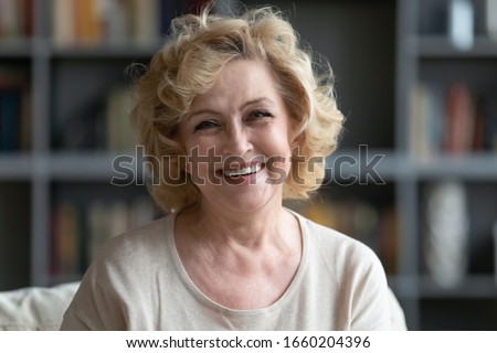 Headshot portrait of positive happy middle-aged 70s Caucasian woman show white healthy teeth, optimistic smiling senior female look at camera posing, relaxing at home, dental care concept
