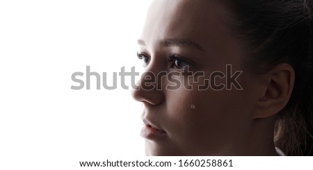 Beautiful young woman with sad big eyes crying. White background. Free space for text. Tear on cheek of unhappy female.