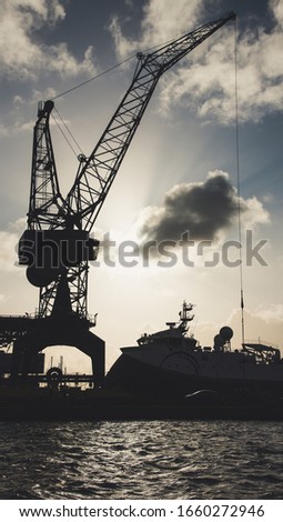 Huge metal dock crane silhouette picture taken during a cloudy day in port. 
