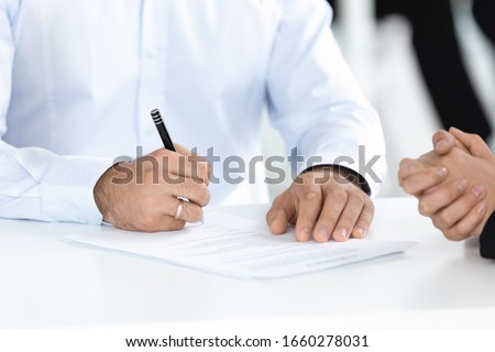 Close up image of man hand putting signature signing paper at meeting concept. Conclusion of agreement with business document, taking bank loan, making financial deal with partner at negotiation.