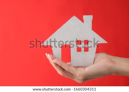 Home purchase concept. Small decorative white house in a hand on a red background