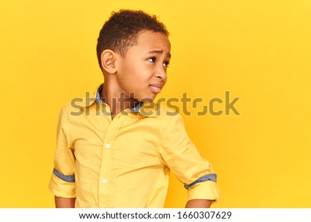 Human facial expressions, attitude and lifes perception. Dissatisfied dark skinned little boy looking away without any interest, feeling bored, having frustrated disappointed look, frowning eyebrows