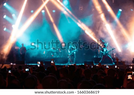 Music fans recording videos on phone in crowd on concert, rear back view of audience people using devices enjoy live music festival event shooting rock band stage on mobile device in blue lights.