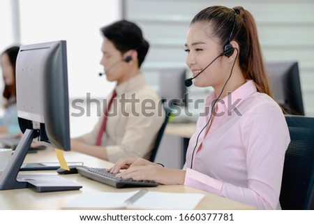 Call center worker accompanied by her team. Smiling customer support operator at work. Young employee working with a headset.
