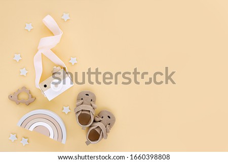 Wooden toys with rainbow, toy camera and cute baby slippers for kids on yellow background.  Set of gender neutral newborn accessories. Flat lay, top view  Royalty-Free Stock Photo #1660398808