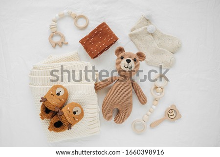 Knitted toy bear, blanket, socks,  and wooden teether for newborn on white bed.  Gender neutral  baby stuff and accessories. Flat lay, top view Royalty-Free Stock Photo #1660398916