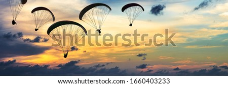 Silhouette Of Paragliders Against Dramatic Sky At Sunset