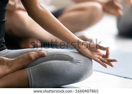 During yoga session group of people seated cross-legged improve self-awareness, increase clarity of mind, close up focus on female folded fingers Gyan mudra sign, no stress meditation practise concept Royalty-Free Stock Photo #1660407865