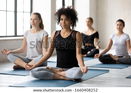 Sporty girls and guys sitting in lotus pose during yoga class led by african woman coach. Group of people do meditation practice, improve inner harmony, healthy lifestyle, mind body relaxation concept Royalty-Free Stock Photo #1660408252