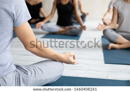 Close up focus on folded fingers mudra gyan sign of male yoga coach sitting in lotus pose on mat during meditation session with group of people. No stress, improve clarity of mind, well-being concept Royalty-Free Stock Photo #1660408261