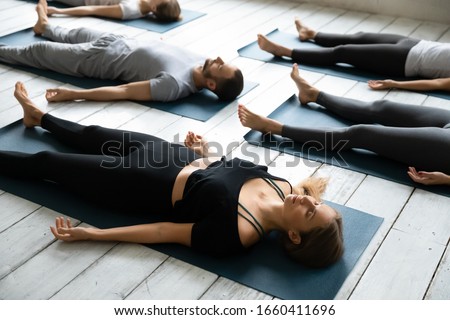 Group of people resting after yoga workout lying in Shavasana Corpse Dead body pose focus on Caucasian girl, relaxation asana, reducing fatigue, improve inner harmony, increase self-awareness concept Royalty-Free Stock Photo #1660411696