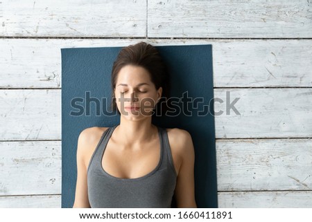 Above top view young woman wearing sports top lying on mat with eyes closed resting after yoga work out do Shavasana Corpse Dead Body posture rejuvenates body mind reducing stress and tension concept Royalty-Free Stock Photo #1660411891