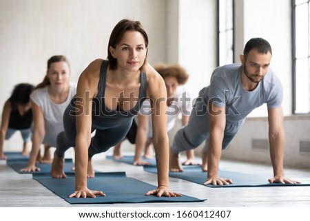 Yoga class led by caucasian woman coach training group of people performing together plank pose, do push up press up exercise strengthens spine and abdominal muscles, work out at club activity concept Royalty-Free Stock Photo #1660412407