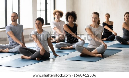 Horizontal image seven multi-ethnic people during yoga class seated in lotus position performing Easy Twist Pose or Parivrtta Sukhasana. Exercise decrease feeling of nervousness, reduce stress concept Royalty-Free Stock Photo #1660412536
