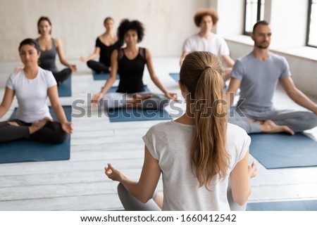 Rear back view woman yoga coach and diverse group of people on background sit in lotus pose do meditation practice, feel sense of calm, peace and inner balance, emotional well-being and health concept Royalty-Free Stock Photo #1660412542