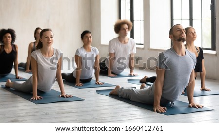 Male instructor and group of diverse people performing Upward Facing Dog during morning work out at yoga class in sport studio, asana strengthens and stretches body, wellness healthy lifestyle concept Royalty-Free Stock Photo #1660412761