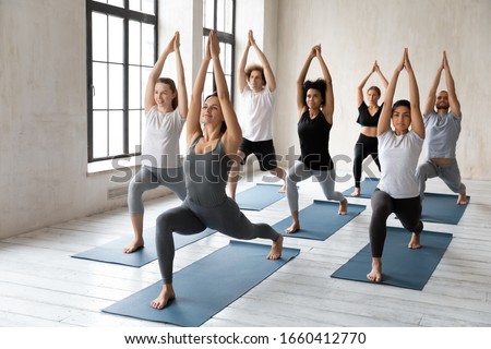 Yoga session led by caucasian woman coach, millennial athletic multiracial group of people practising posture with female instructor, doing Warrior one Virabhadrasana I asana, workout full length view Royalty-Free Stock Photo #1660412770