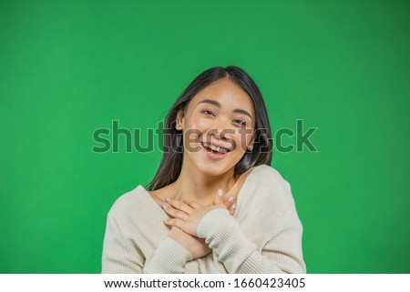 Beautiful, positive, friendly looking young Asian woman with a lovely sincere smile, feeling gratitude and gratitude, showing her heart filled with love and gratitude, holding hands on her chest