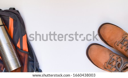 Boots, a thermos and a backpack. Concept on the topic of active lifestyle. Free space for text. Horizontal photo. Light background.