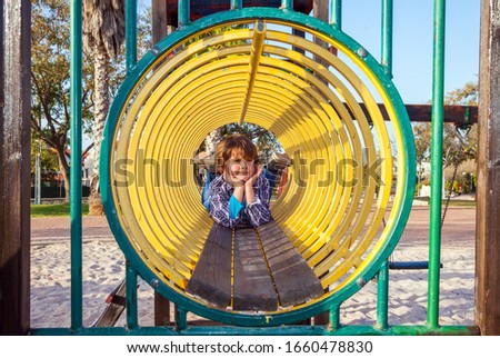 Children playground. Beautiful sunny day. Handsome and charming boy in a plaid cowboy shirt creeps along the tubular passage. Concept of photo advertising and happy childhood