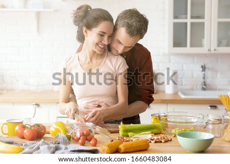 Husband hug loving caring smiley wife chopping veggie for salad on cutting board. Overjoyed cute family couple cooking together on kitchen. Loving newlywed married man and woman portrait Royalty-Free Stock Photo #1660483084