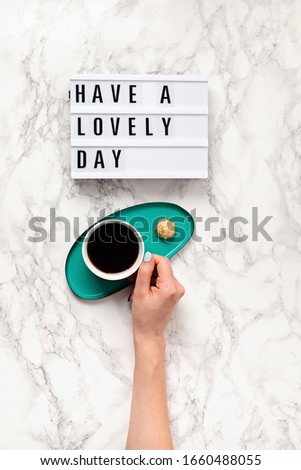 Flat lay with lightbox with text "Have a lovely day" and coffee cup in woman hand. Social media, motivation quote, feminine blog, morning of workday concept