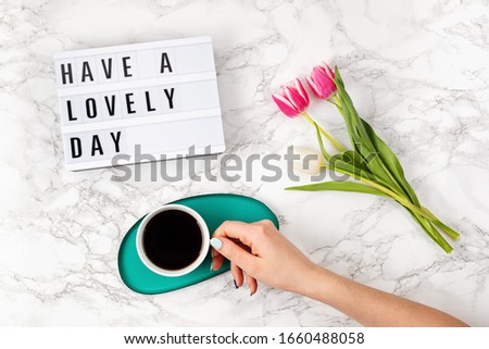 Flat lay with lightbox with text "Have a lovely day" and coffee cup in woman hand. Social media, motivation quote, feminine blog, morning of workday concept