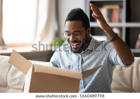 Head shot handsome young african american man opening cardboard parcel, feeling excited about getting wished item from internet store. Happy multiracial male client unpacking delivery box at home. Royalty-Free Stock Photo #1660489798