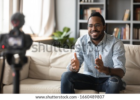 Happy young african american man speaker in eyewear sitting in front of camera, recording educational video webinar training at home. Smiling skilled biracial guy introducing for job interview. Royalty-Free Stock Photo #1660489807
