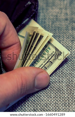 black wallet with dollars in the hands on grey background. financial wellness. copy space. vertical photo. toned