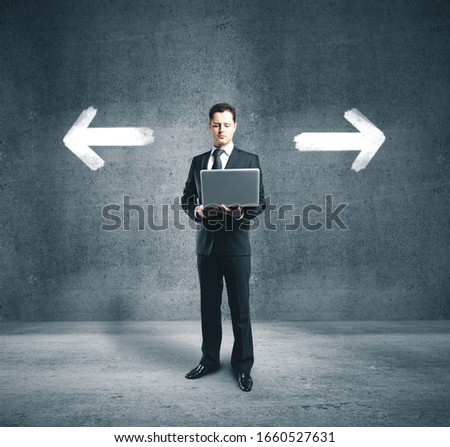 Businessman holding laptop and two drawing white arrow on concrete wall. Business and success concept