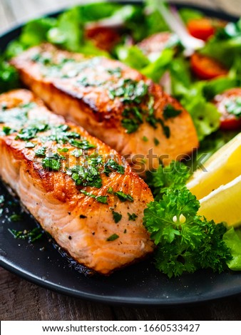 Fried salmon steaks with vegetables on wooden table Royalty-Free Stock Photo #1660533427