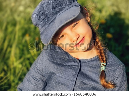 Happy smiling kid girl looking on the glass in blue clothing on summer green background. Closeup portrait