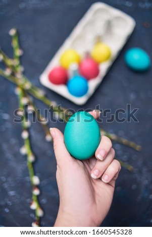 Happy Easter. Painted multi-colored. The girl holds an empty colored egg, a place for text, a picture. Girl shows a colored egg. Blossoms of pussy-willow seals, on an abstract background of dark color