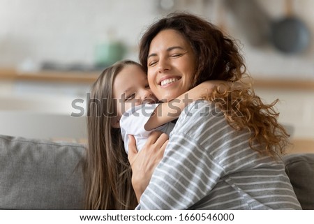 Overjoyed young mother relax on couch have fun cuddling with cute little preschooler daughter at home, happy smiling mom and small funny girl child have fun hug and embrace rest together on sofa Royalty-Free Stock Photo #1660546000