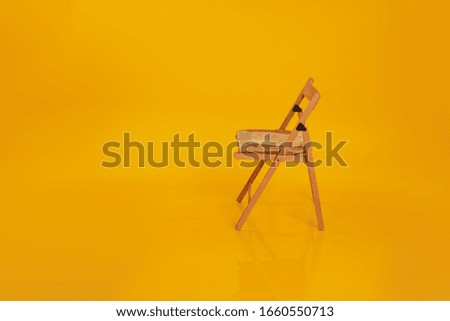 A light wooden chair stands on a yellow background