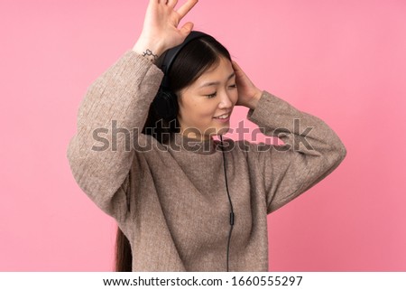 Young asian woman isolated on pink background listening music and dancing
