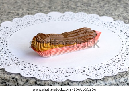 Cake eclair with chocolate cream and milk chocolate cap on a white napkin