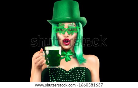 St. Patrick's Day leprechaun laughing model girl holding Green Beer pint, isolated on black background.  Shamrock leaf accessories. Celebrating Patrick Day pub party. Surprised young woman in costume