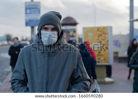 Man in the city. on the face a protective rag mask. remedy against viruses and diseases. protection against coronovirus. There are many passers-by on the street. Bus stop Royalty-Free Stock Photo #1660590280