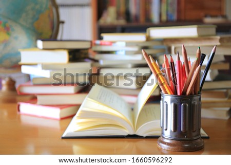 Many colored pencils in the pencil holder on the table in the library Stacks of books and globes in the background selective focus and shallow depth of field