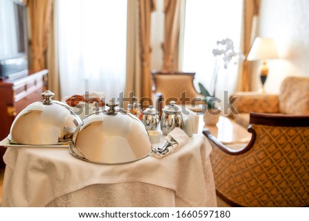 Luxurious Room Service. Breakfast in luxury hotel room delivered by waiter. Meals under silver cloche. Hospitality and vacation concept. Horizontal shot Royalty-Free Stock Photo #1660597180