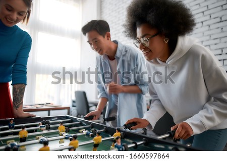 Group of young and happy multicultural people in casual wear playing table soccer in the creative office. Office activities. Having fun together. Happy employees Royalty-Free Stock Photo #1660597864