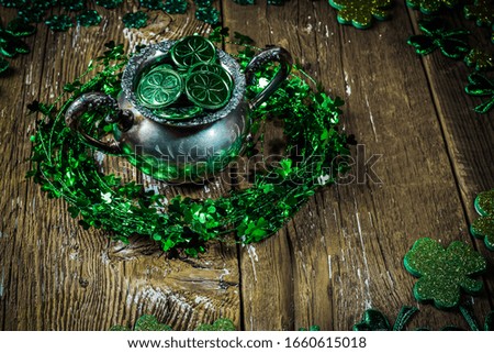 St.Patrick's day holiday symbol. Shamrock wreath, shamrocks and antique silver potty filled with coins on an old rustic wood background. Close up view. Bokeh.