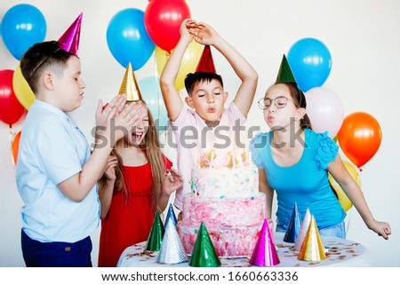 Bright, cute children celebrate a birthday. Multinational party, balloons, caps, smiles, teens near the table with a cake.