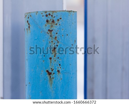 A rusty metal pipe, Rust through the blue paint on an iron post.