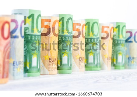 Many euro banknotes stand side by side against a white background